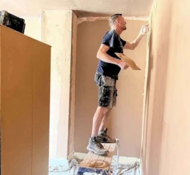 Close-up of a SE London plasterer using a hawk and trowel to finish a wall corner.